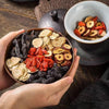 Hands holding a bowl of dried Ginseng tea herbs, showcasing the authentic and natural texture of this premium herbal blend.