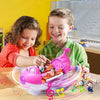 Two young children smiling and interacting with the open-cabin musical airplane toy on a wooden table setup.
